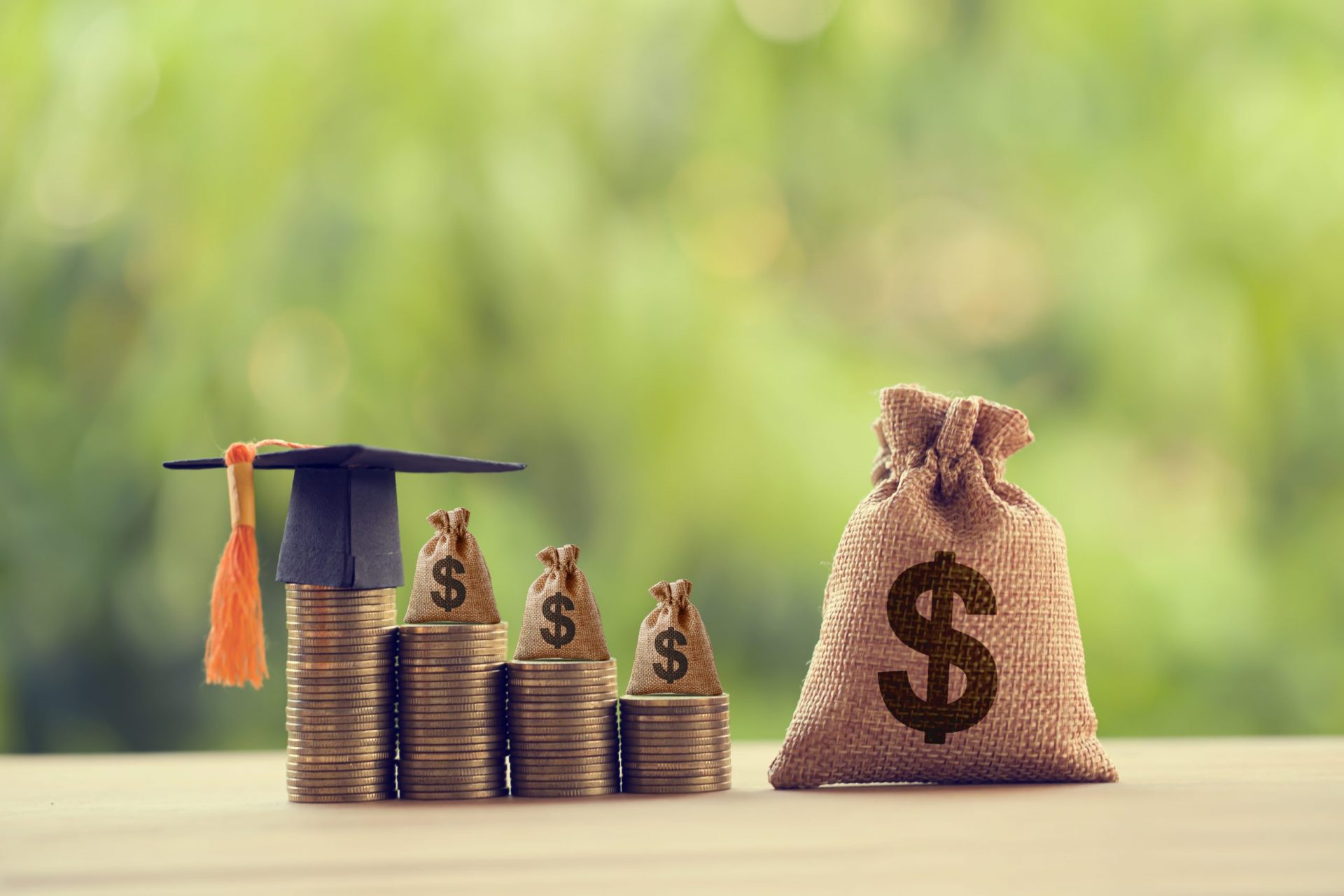 Black graduation cap, Hat and US dollar bag on rows of rising coins, on a table. Education funding, financial concept. Depicts savings for child knowledge for future studies