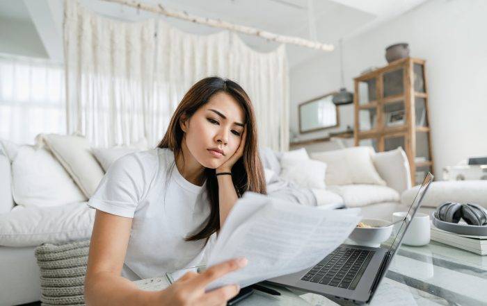 Stressed and worried young Asian woman working from home, handling paperworks and going through her financials