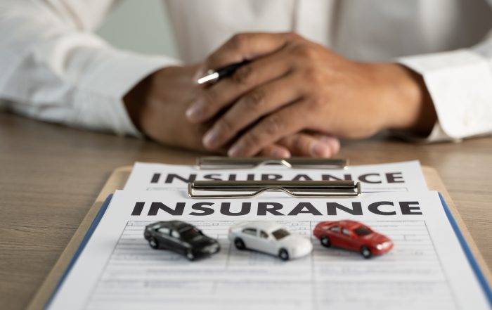 Man sitting at a desk with hands folded in front of insurance paperwork and small toy cars