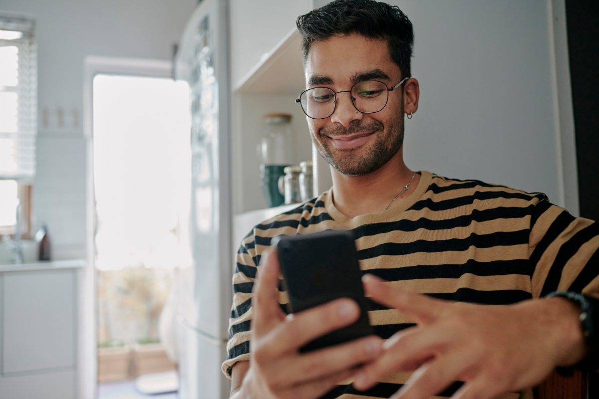 Expert Nearby from home, phone in kitchen (iStock 1555725251) A man smiling at his phone in his kitchen